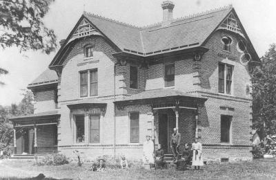 Two story house with Victorian details and three family members out front.